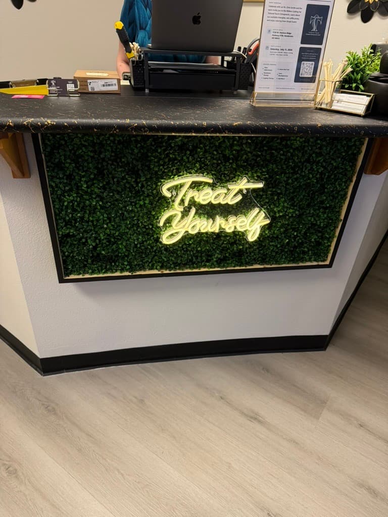 'Treat Yourself' neon sign on the greenery wall at the Tailored Touch reception desk